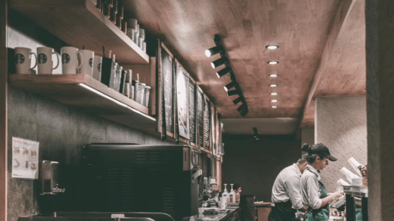 Barista atendendo no balcão de uma cafeteria moderna enquanto utiliza máquina de café profissional em ambiente comercial iluminado