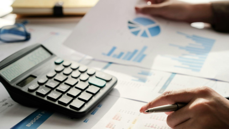 Plano detalhado de uma pessoa analisando relatórios financeiros sobre uma mesa de trabalho bem iluminada.