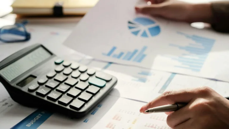 Plano detalhado de uma pessoa analisando relatórios financeiros sobre uma mesa de trabalho bem iluminada.
