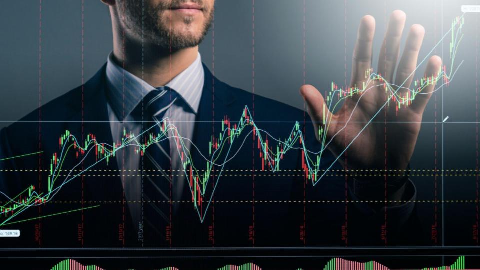 A imagem mostra um homem de negócios interagindo conceitualmente com uma tela sensível ao toque contendo dados e gráficos do mercado financeiro.