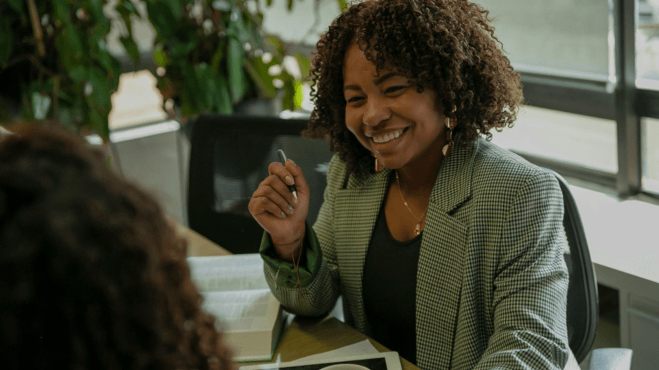 Uma profissional sorridente conversa com uma colega numa reunião individual de trabalho.