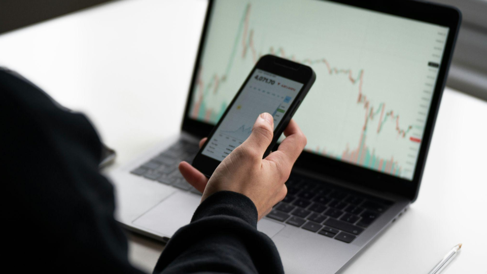 Close-up em um smartphone exibindo um aplicativo de investimentos com fundo escuro.
