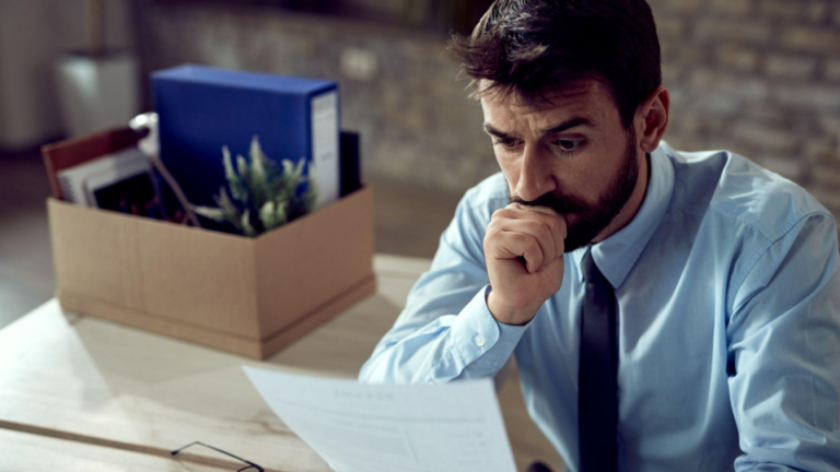 A imagem retrata um homem em um momento de preocupação ou apreensão relacionado ao seu trabalho, sugerindo uma demissão ou momento financeiro difícil.